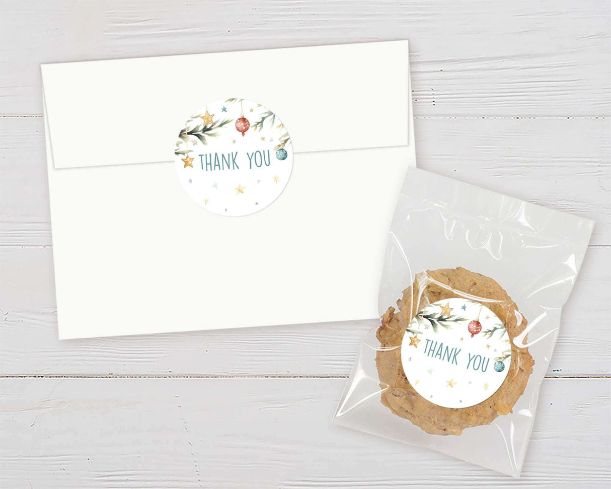 Christmas baby shower favor with thank you sticker featuring holiday ornaments and stars on an envelope and cookie bag.