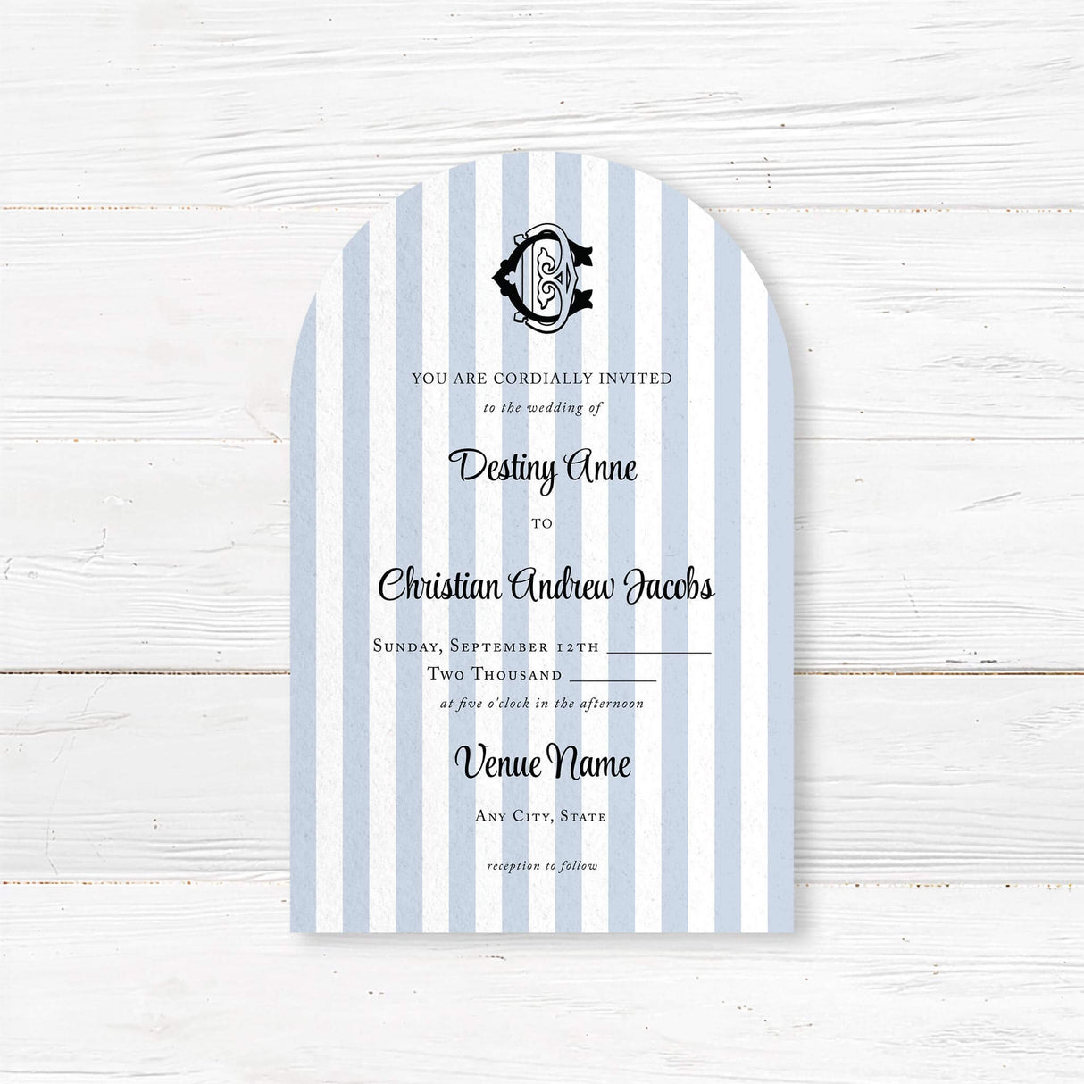 Arched wedding invitation with vertical light blue and white stripes, elegant black crest monogram at the top, and a mix of serif and script fonts for a classic and refined look, ideal for coastal or nautical wedding themes.