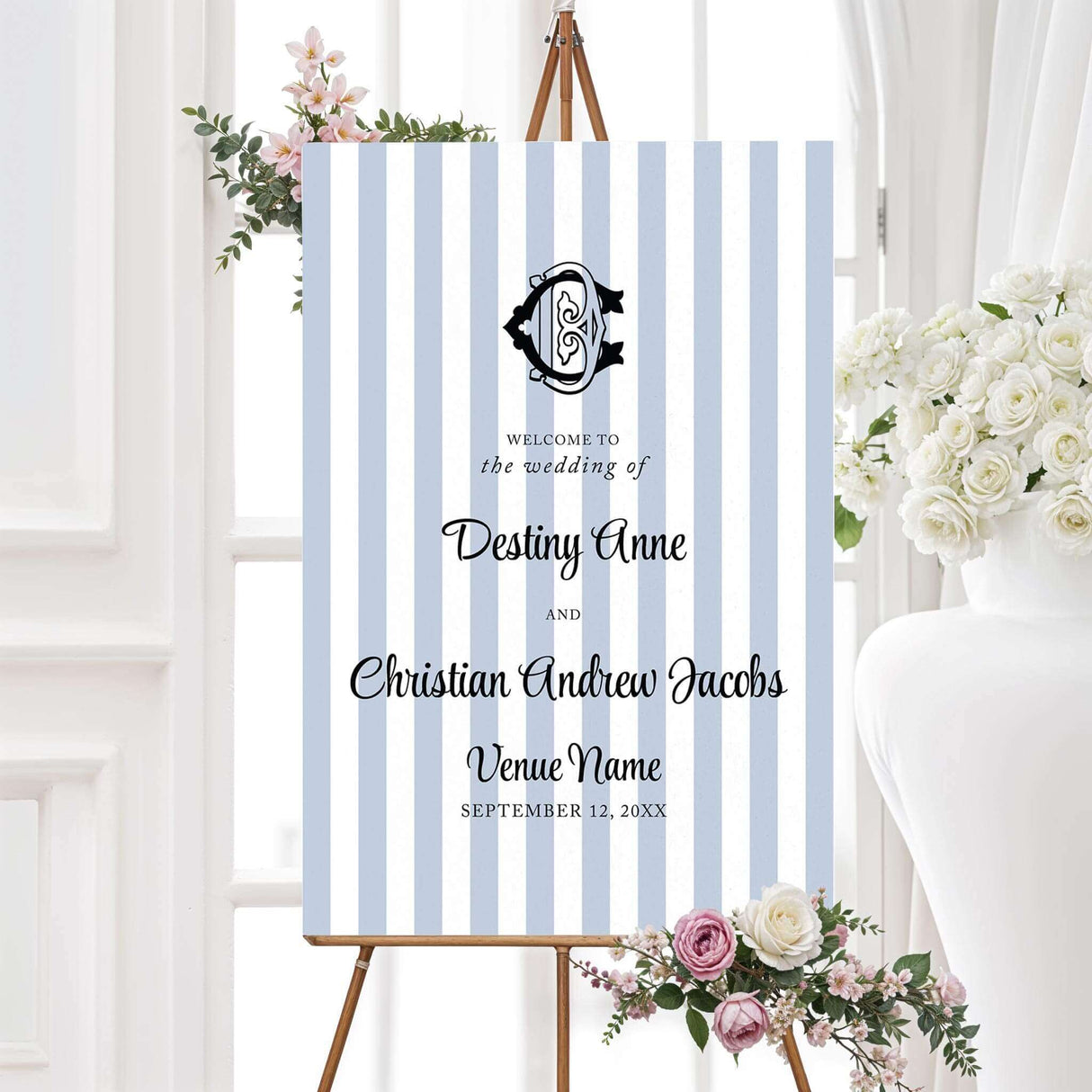 Wedding welcome sign with soft blue and white stripes and a striking monogram crest at the top, perfect for a refined, coastal, or preppy wedding entrance.