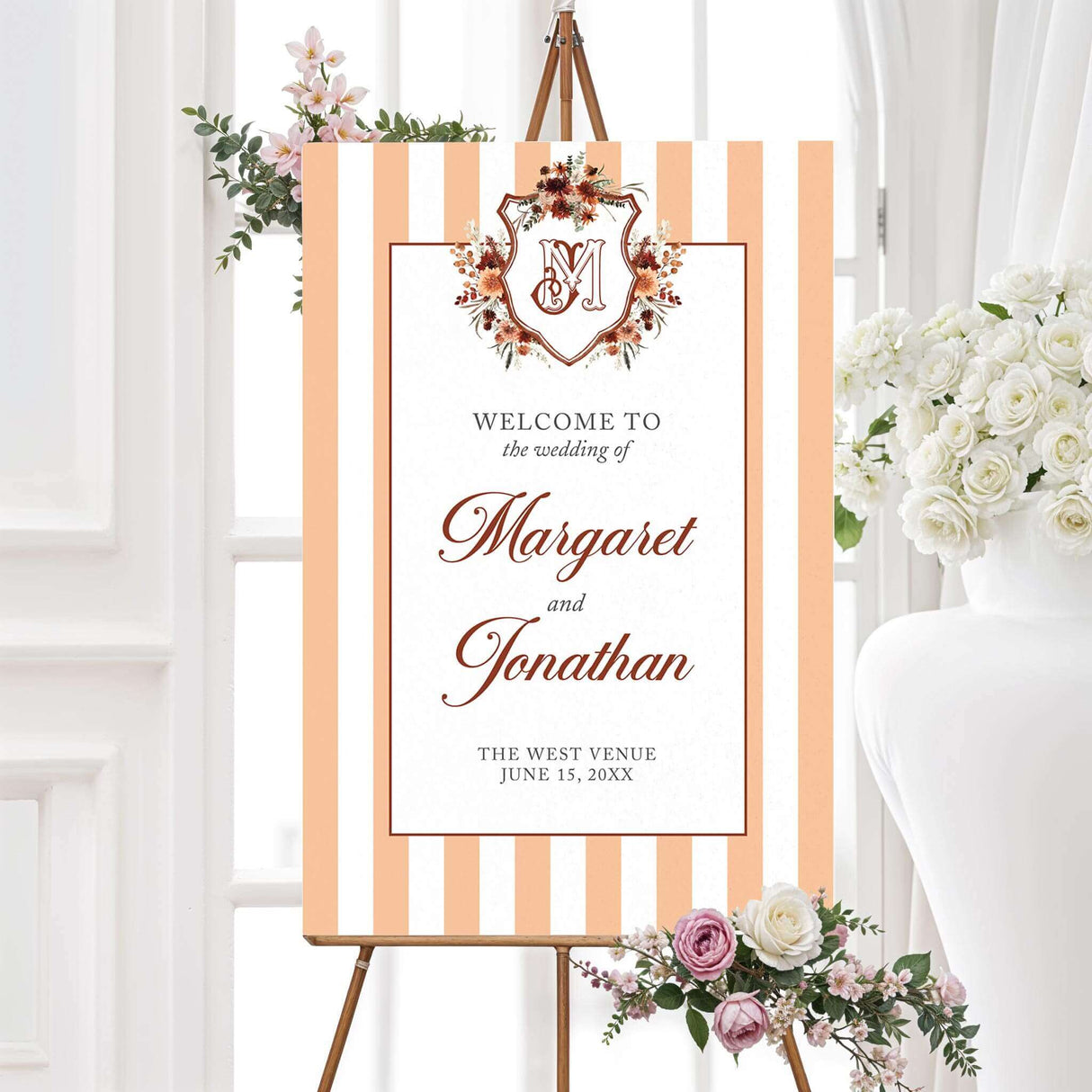 Wedding welcome sign with floral monogram crest, vertical peach and terracotta stripes, and matching fonts, designed to coordinate with an elegant autumn wedding stationery suite.