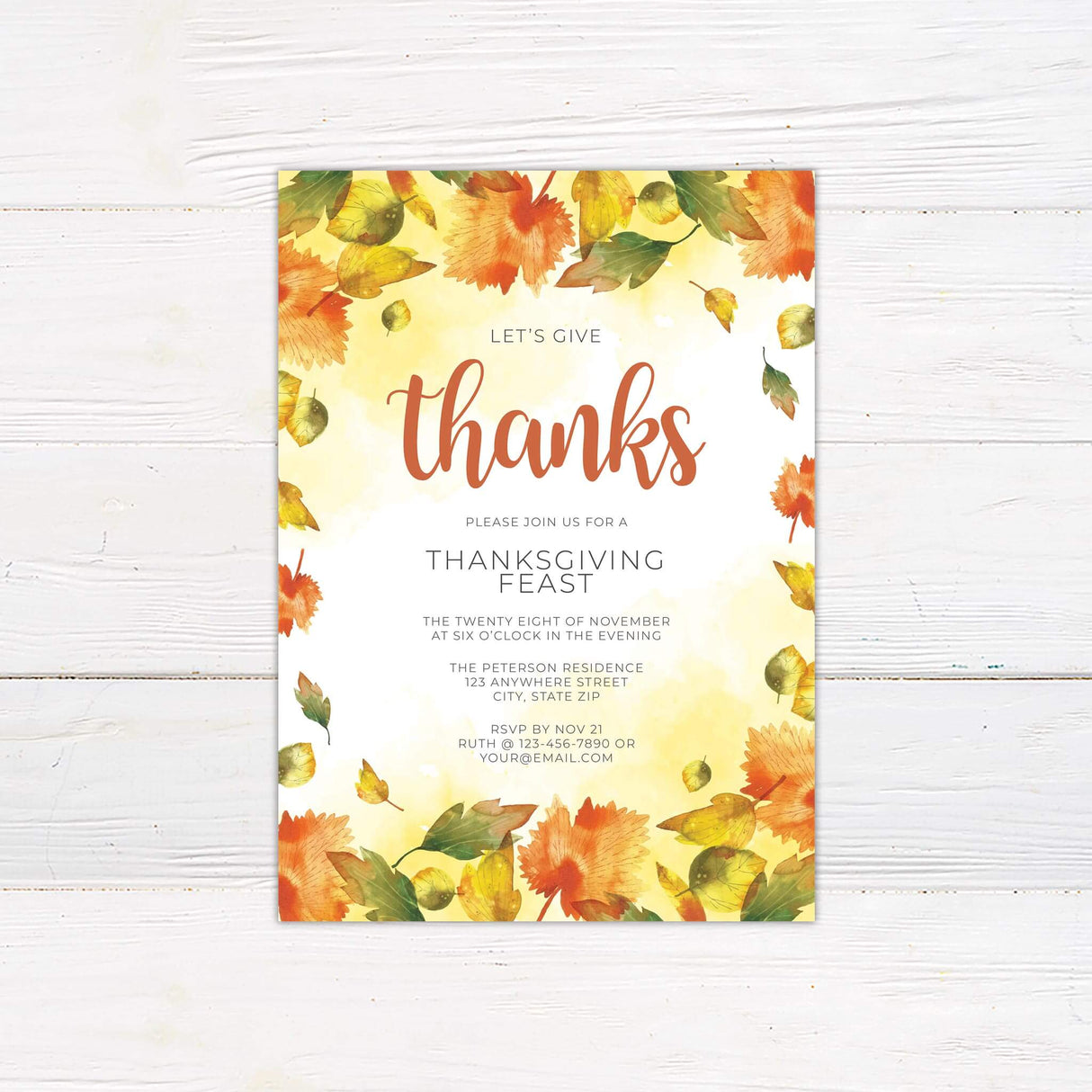 Autumn Leaves Give Thanks invitation for Thanksgiving feast with orange and yellow leaf design on white wooden background.