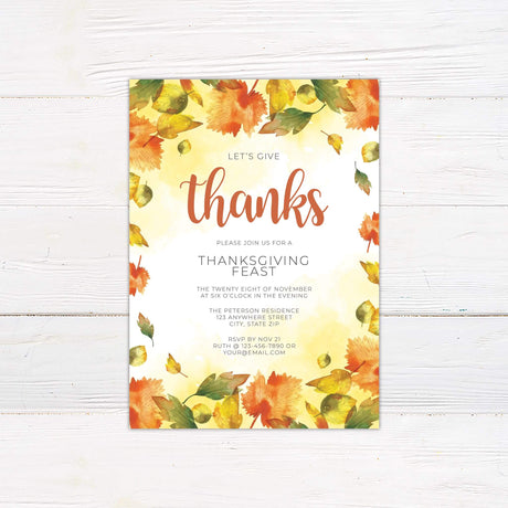 Autumn Leaves Give Thanks invitation for Thanksgiving feast with orange and yellow leaf design on white wooden background.