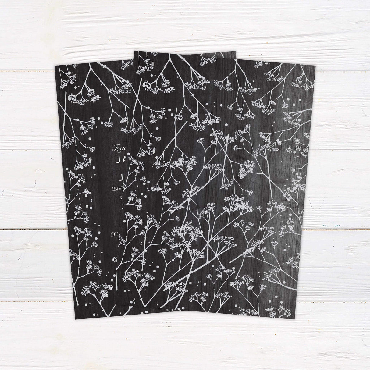 Rustic wedding invitation with dark wood background, white baby's breath floral accents, and elegant script and serif fonts for an outdoor or barn wedding. back