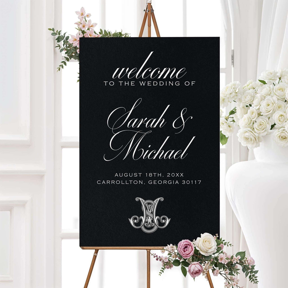 Black Celtic Monogram Wedding Invitation with script fonts on easel, surrounded by flowers, featuring elegant white calligraphy.