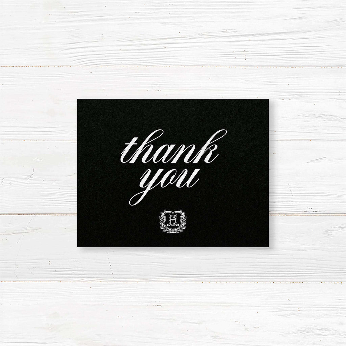 Black Wreath Shield Wedding Invitation - Wedding thank you card with black background, white calligraphy fonts, and an ornate shield monogram encircled by a laurel wreath, matching a formal black wedding suite.-