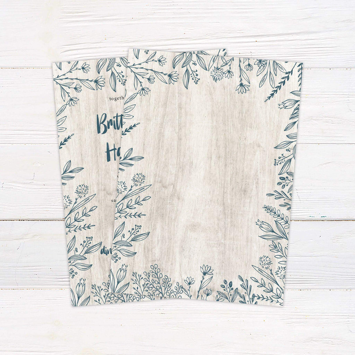 Rustic wedding invitation with hand-drawn blue floral frame and woodgrain background, featuring a blend of script and serif fonts. - back