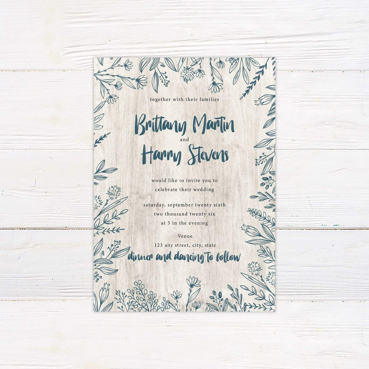 Rustic wedding invitation with hand-drawn blue floral frame and woodgrain background, featuring a blend of script and serif fonts.