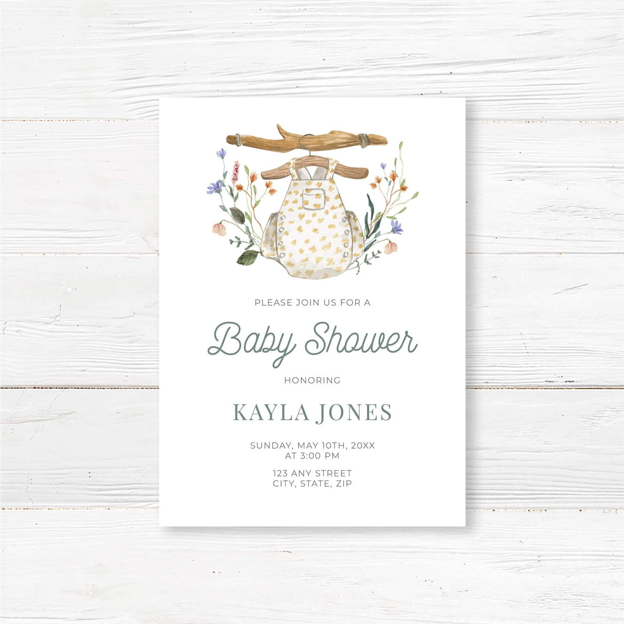 Printed boho baby shower invitation featuring a soft watercolor baby romper on a rustic wooden hanger, surrounded by wildflowers. This elegant and gender-neutral invitation is perfect for a bohemian baby shower, woodland baby sprinkle, or floral country baby shower. Professionally printed on high-quality cardstock with envelopes included. Fully customizable with honoree’s name, date, location, and registry details.