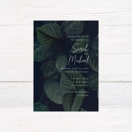 Elegant wedding invitation featuring dark green watercolor leaves with modern script text for a botanical evening wedding