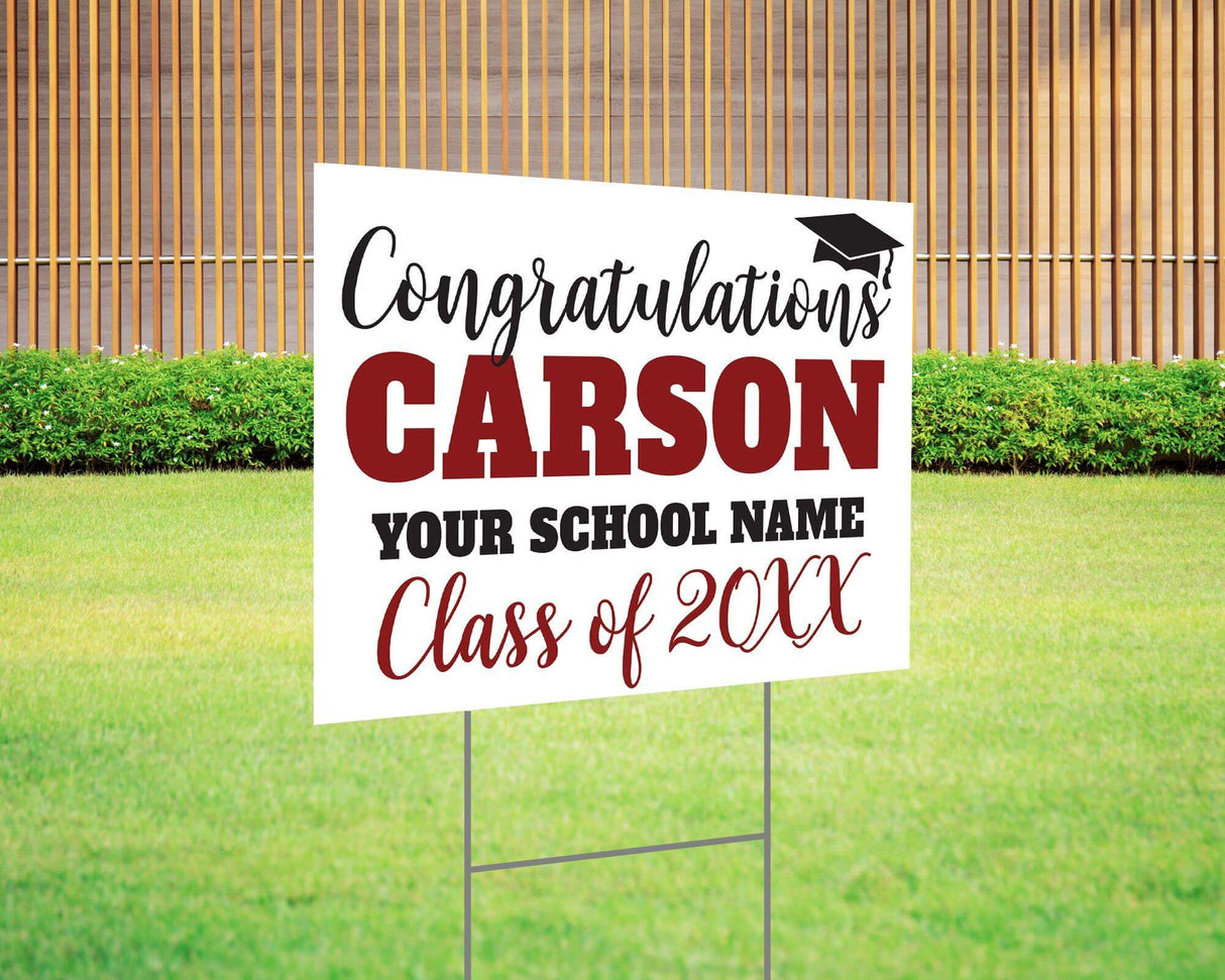 Custom graduation yard sign with bold name design in maroon and black, featuring a congratulatory message, a graduation cap graphic, and customizable school name and class year. Printed on durable Coreplast plastic, available in single or double-sided options. Perfect for high school and college graduates.