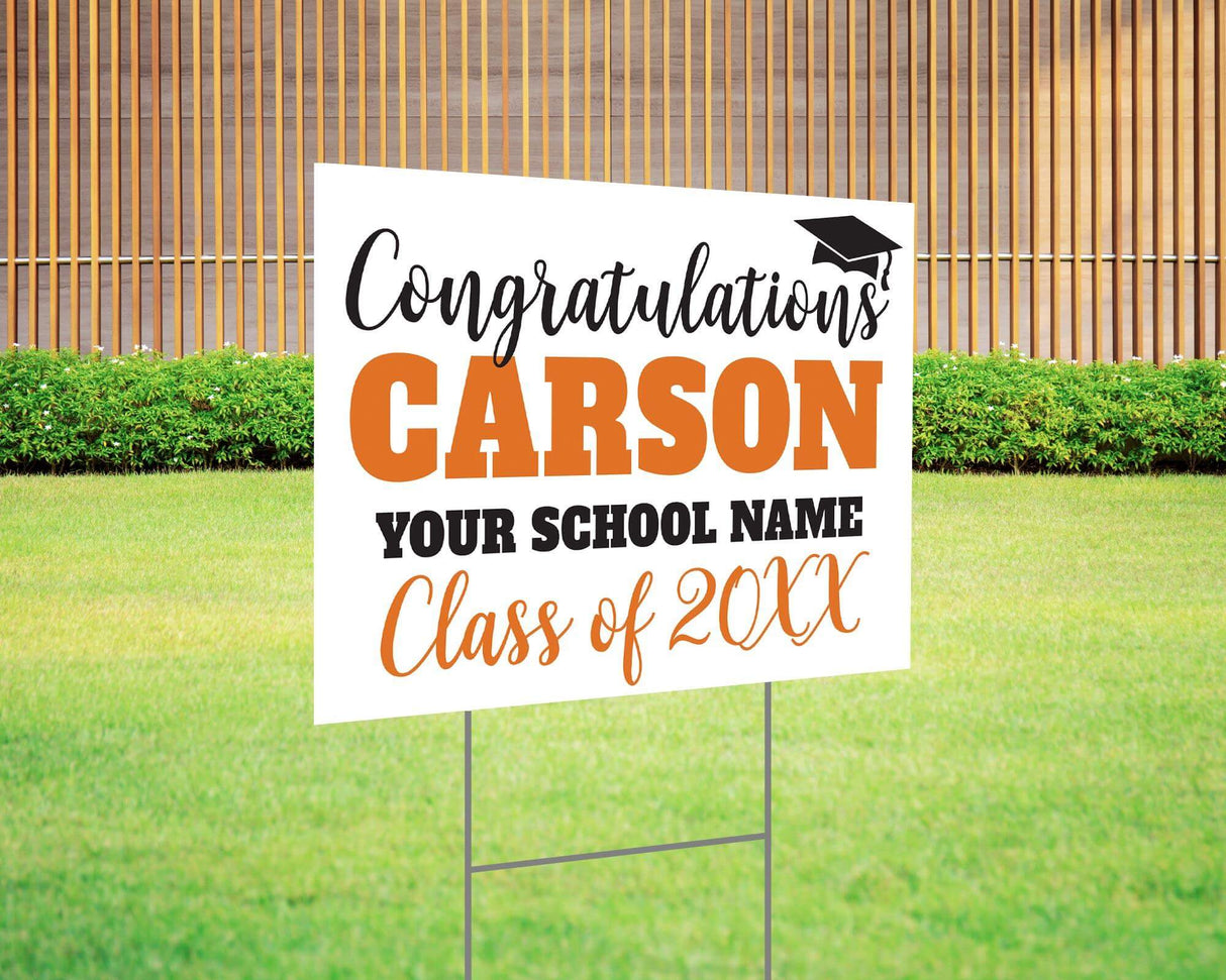 Custom graduation yard sign with bold name design in orange and black, featuring a congratulatory message, a graduation cap graphic, and customizable school name and class year. Printed on durable Coreplast plastic, available in single or double-sided options. Perfect for high school and college graduates.