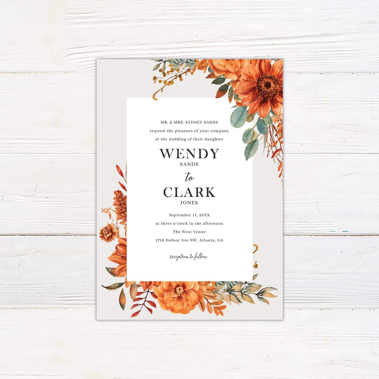 A wedding invitation with a neutral background features vibrant watercolor florals in warm autumn tones of orange, gold, and green framing the design. The text is centered within a white rectangular box, using a mix of serif and script fonts for a classic and elegant feel. Event details, including the date, time, and venue, are clearly displayed in a structured layout. This design exudes warmth and sophistication, perfect for a fall or rustic-themed wedding celebration.