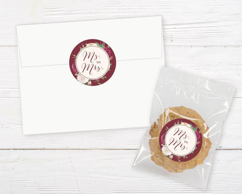 A burgundy rose floral bridal shower invitation sticker with roses and elegant script text. The design features deep red and blush flowers on a dark background.
