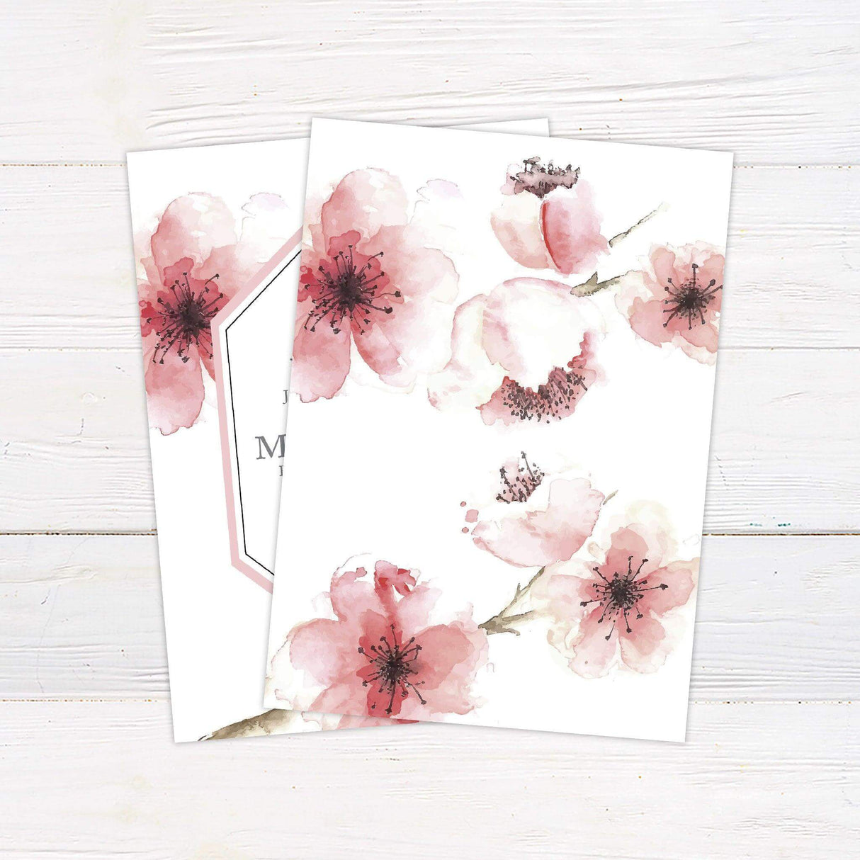 Wedding invitation with blush pink cherry blossom watercolor background and modern geometric frame, featuring serif and script text on a white backdrop. - back