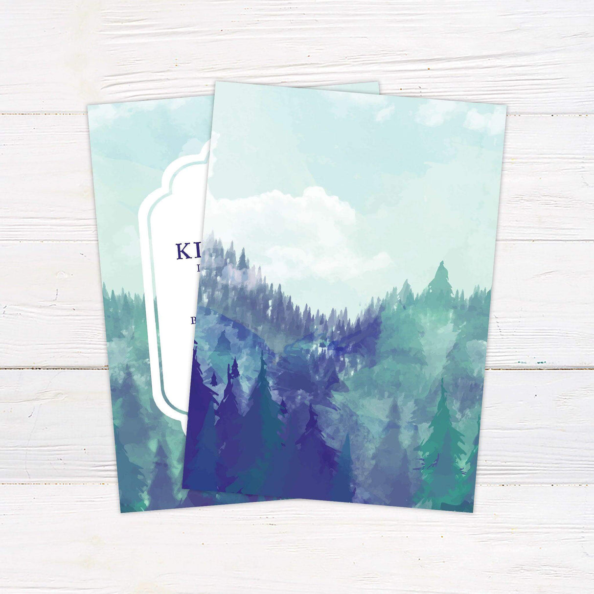 Wedding invitation featuring a misty watercolor mountain and forest background with elegant typography framed in a white ornate border. back