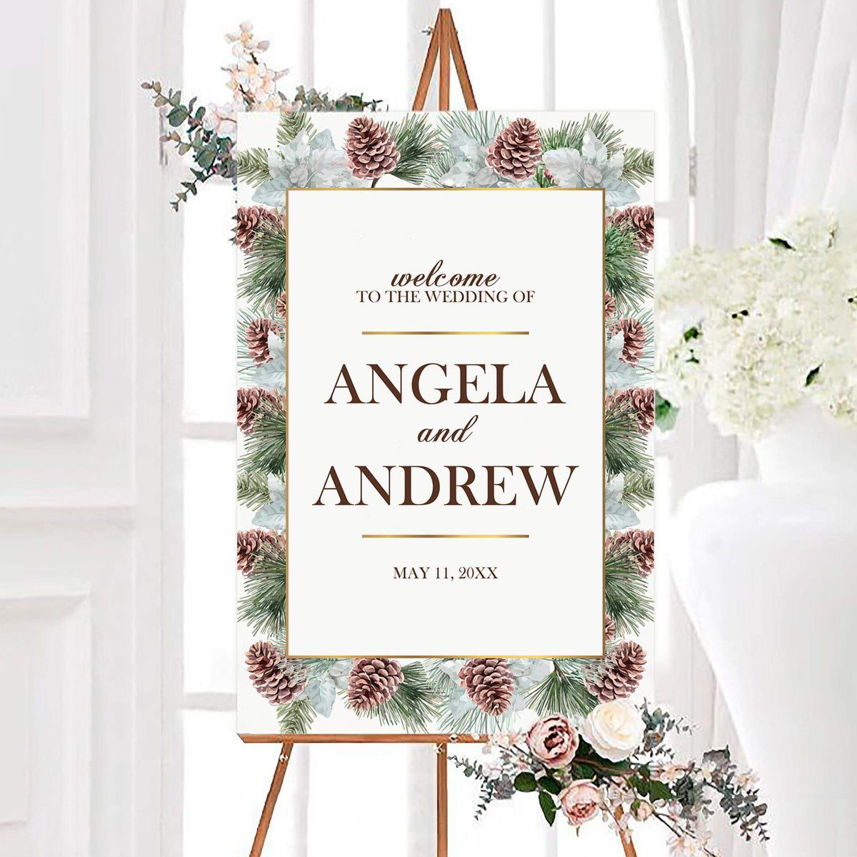 Personalized conifer cone wedding welcome sign surrounded by evergreen branches, pinecones, and frosted botanical accents. The center features the couple's names and wedding date in elegant typography.