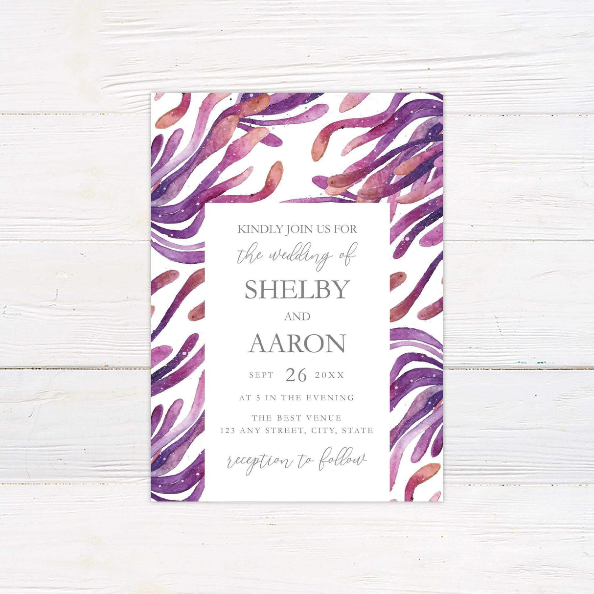 Modern wedding invitation with watercolor brushstrokes in purple, coral, and plum, featuring a central white panel with elegant serif and script text.