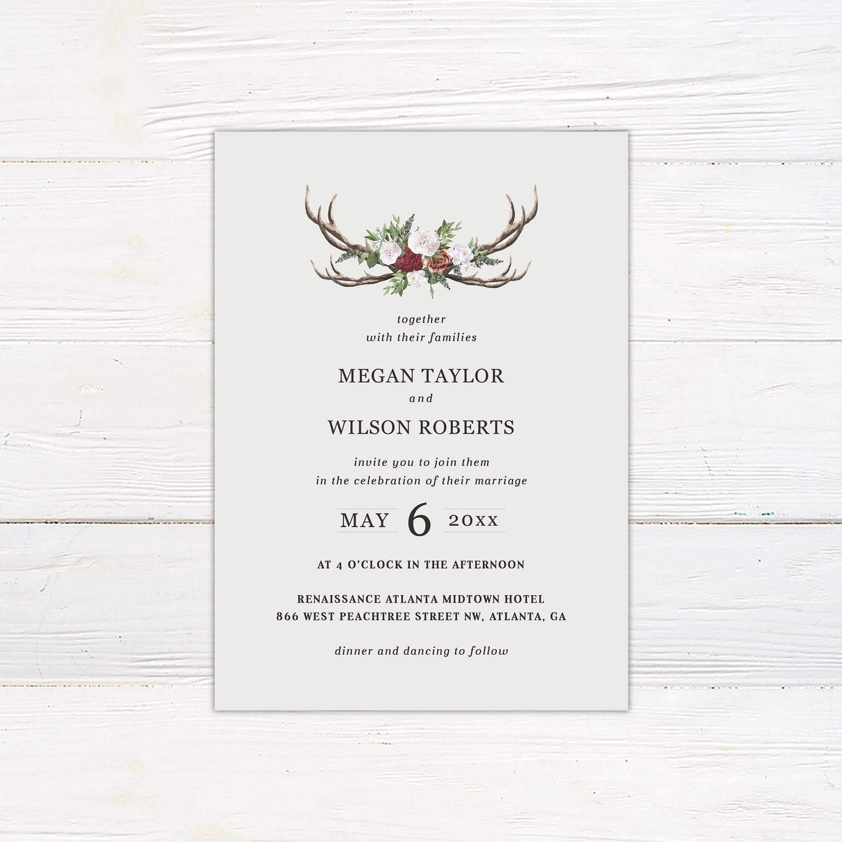 Wedding invitation with watercolor antlers, burgundy and white roses, greenery, and serif typography on a light cream background