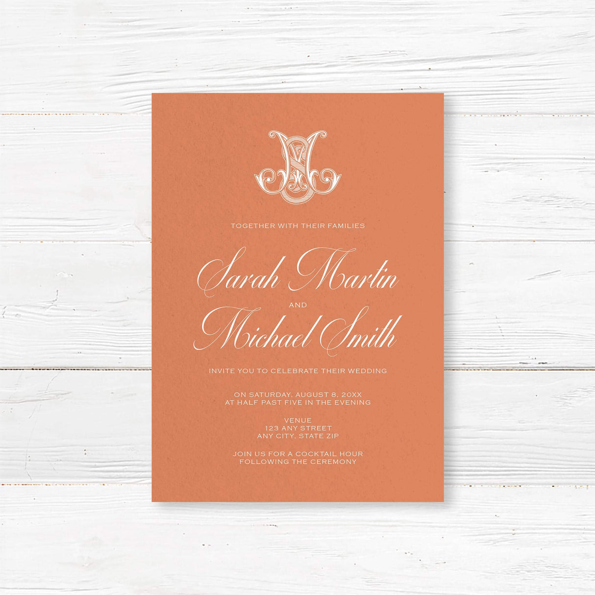 Terracotta wedding invitation with white calligraphy and ornate Celtic-style monogram