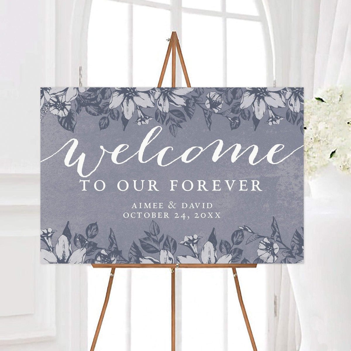 Vintage distressed blue wedding welcome sign with a distressed background and illustrated botanical borders. The sign reads “Welcome to Our Forever” and is personalized with the couple’s names and wedding date.