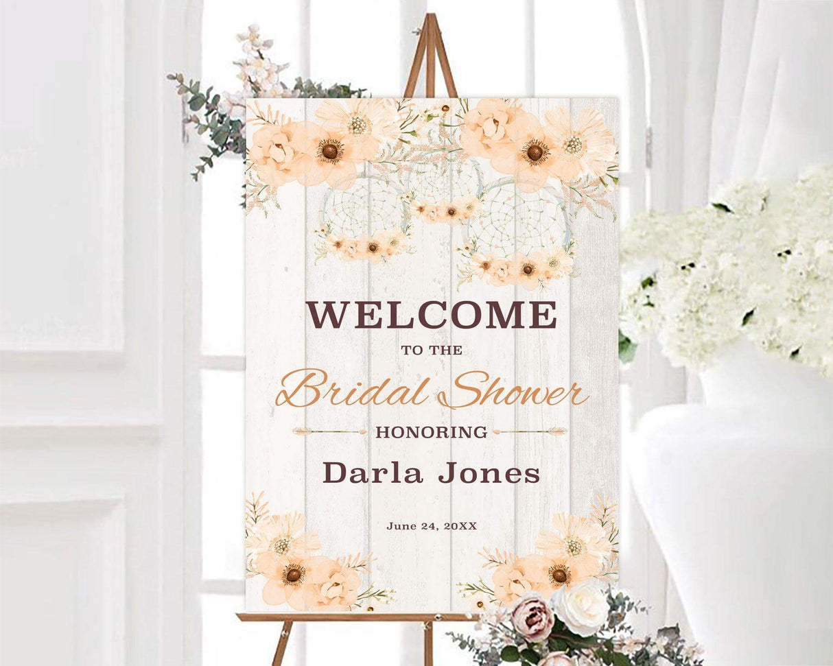 A bridal shower sign with peach flowers and a dream catcher design. The background has a light rustic wood texture.