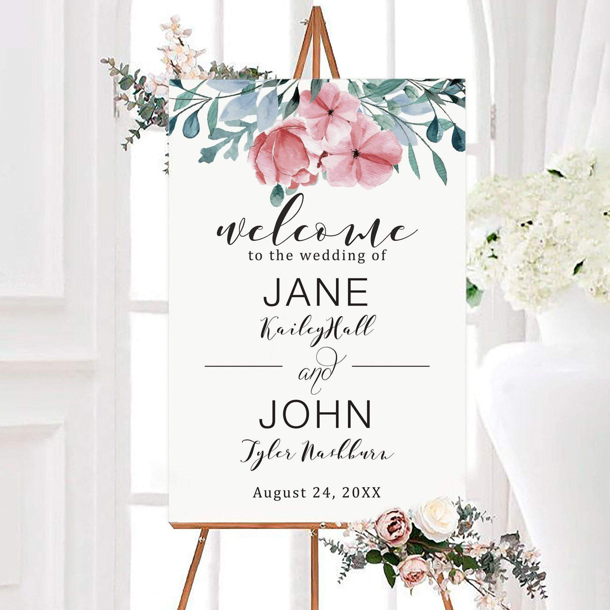 Watercolor dusty blue diamond wedding welcome sign with soft flowers and leafy greenery across the top. The personalized sign features the couple’s names and wedding date in elegant typography.