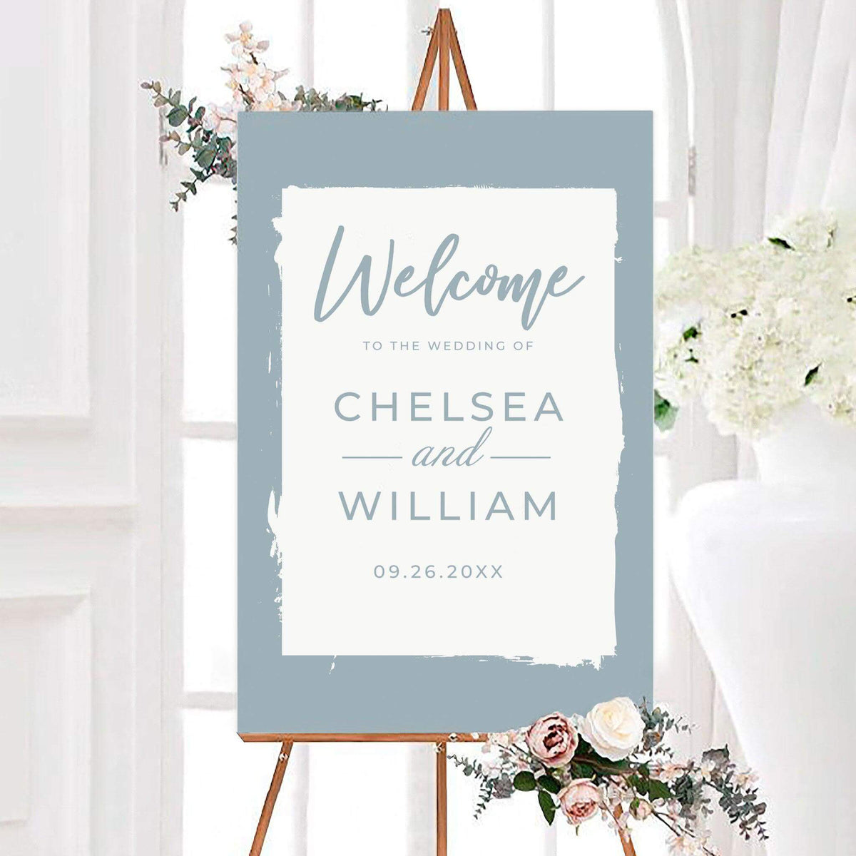 Modern dusty blue wedding welcome sign featuring an artistic brushstroke border and clean contemporary typography. The sign is personalized with the couple’s names and wedding date.