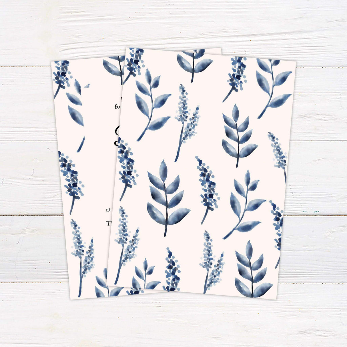 Elegant wedding invitation with blue watercolor leaves and berries framing black script text on a cream background - back