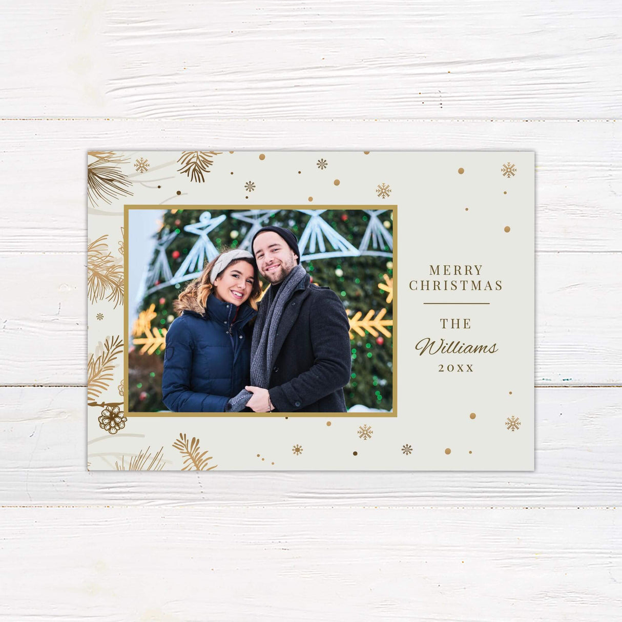Custom holiday card with a gold frame for a photo, cream background decorated with pine branches and snowflakes, and Merry Christmas text with family name.