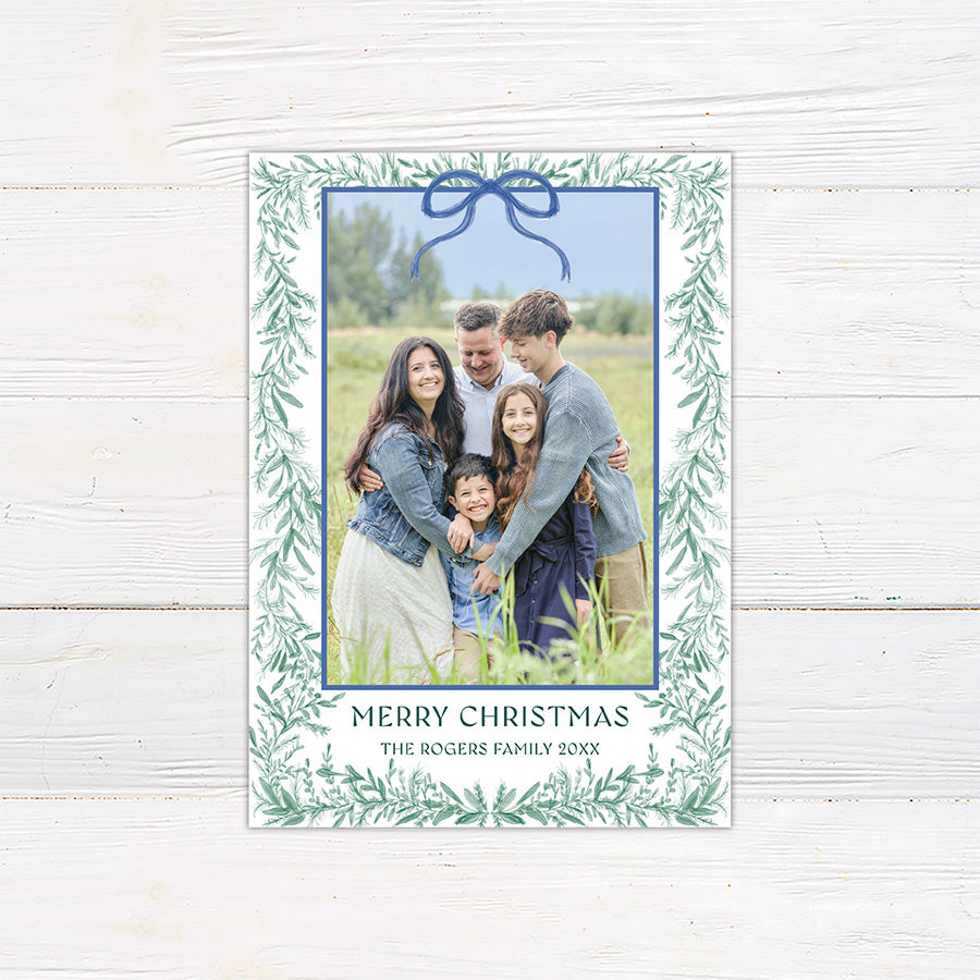 Personalized family Christmas photo card framed with delicate watercolor greenery and an elegant bow.