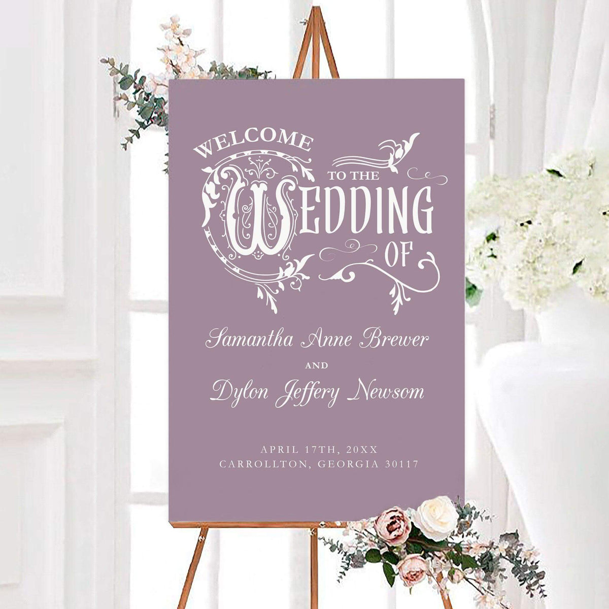 Enchanted wedding welcome sign featuring ornate white typography, decorative flourishes, and personalized couple names. The design includes the wedding date beneath the names on a solid background.