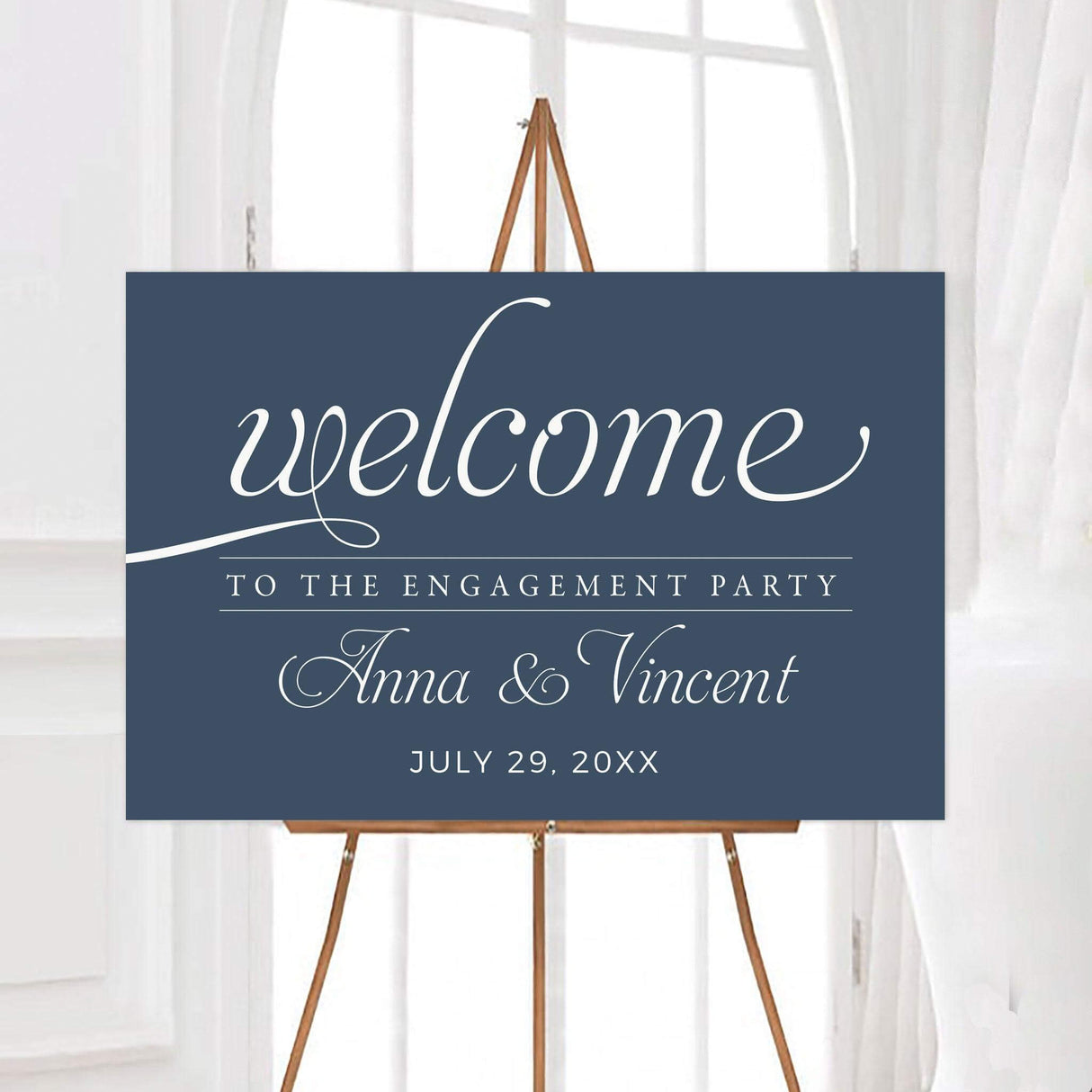 Elegant engagement party welcome sign with calligraphy text on a blue background, featuring a wooden easel in a bright room.