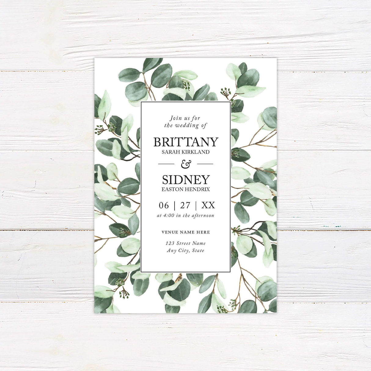 A wedding invitation with a white background features a lush greenery design of watercolor eucalyptus leaves framing the layout. The text is centered within a clean, black-bordered rectangle, using a mix of serif and script fonts for an elegant and modern touch. Event details, including the date, time, and venue, are clearly displayed in a structured format. This design exudes natural simplicity and sophistication, making it perfect for a botanical, minimalist, or rustic wedding celebration.