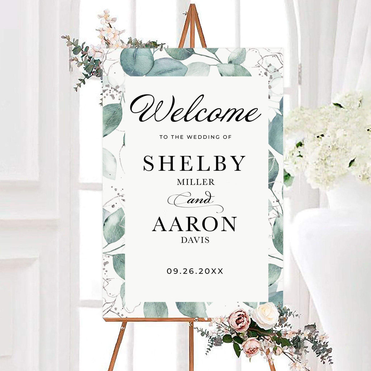Personalized eucalyptus splash wedding welcome sign framed with watercolor eucalyptus leaves and delicate floral outlines. Elegant typography displays the couple’s names and wedding date in the center.