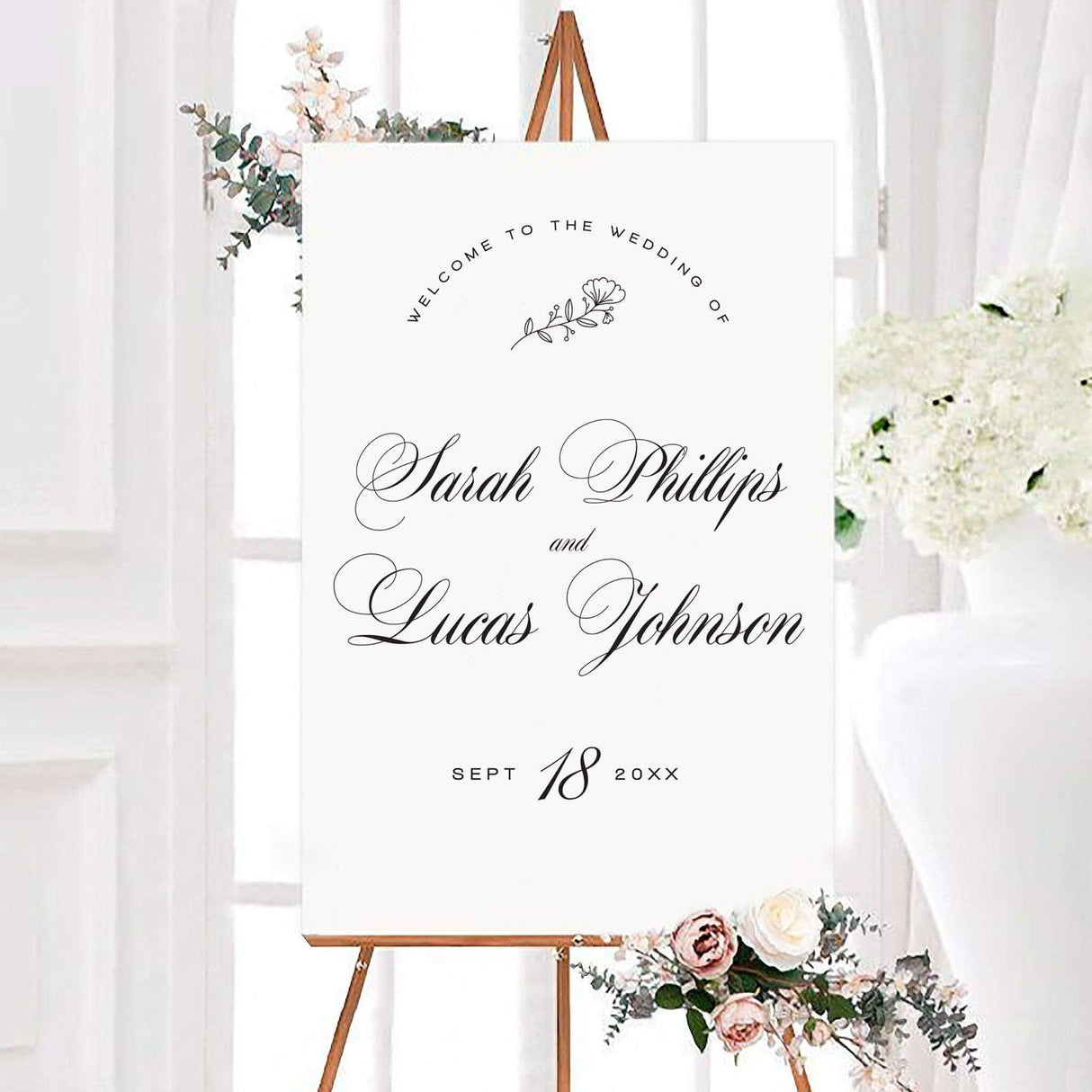 Elegant black and white fancy script wedding welcome sign featuring personalized names in large fancy script calligraphy. A delicate floral sprig, arched welcome text, and custom wedding date complete the minimalist design.