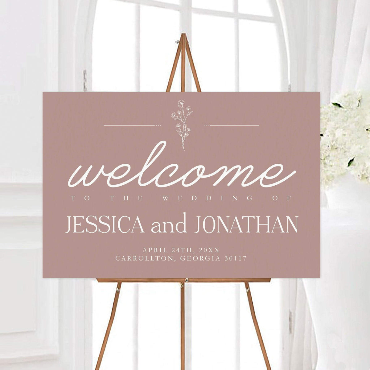 Elegant floral accent wedding welcome sign featuring flowing script lettering and a delicate line-art wildflower accent. The sign includes personalized couple names, wedding date, and location.