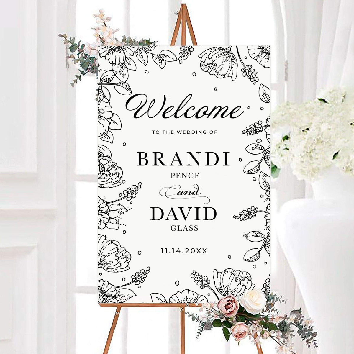 Black and white floral sketch wedding welcome sign featuring hand-drawn flowers and leaves around the border. Personalized typography displays the couple’s names and wedding date.