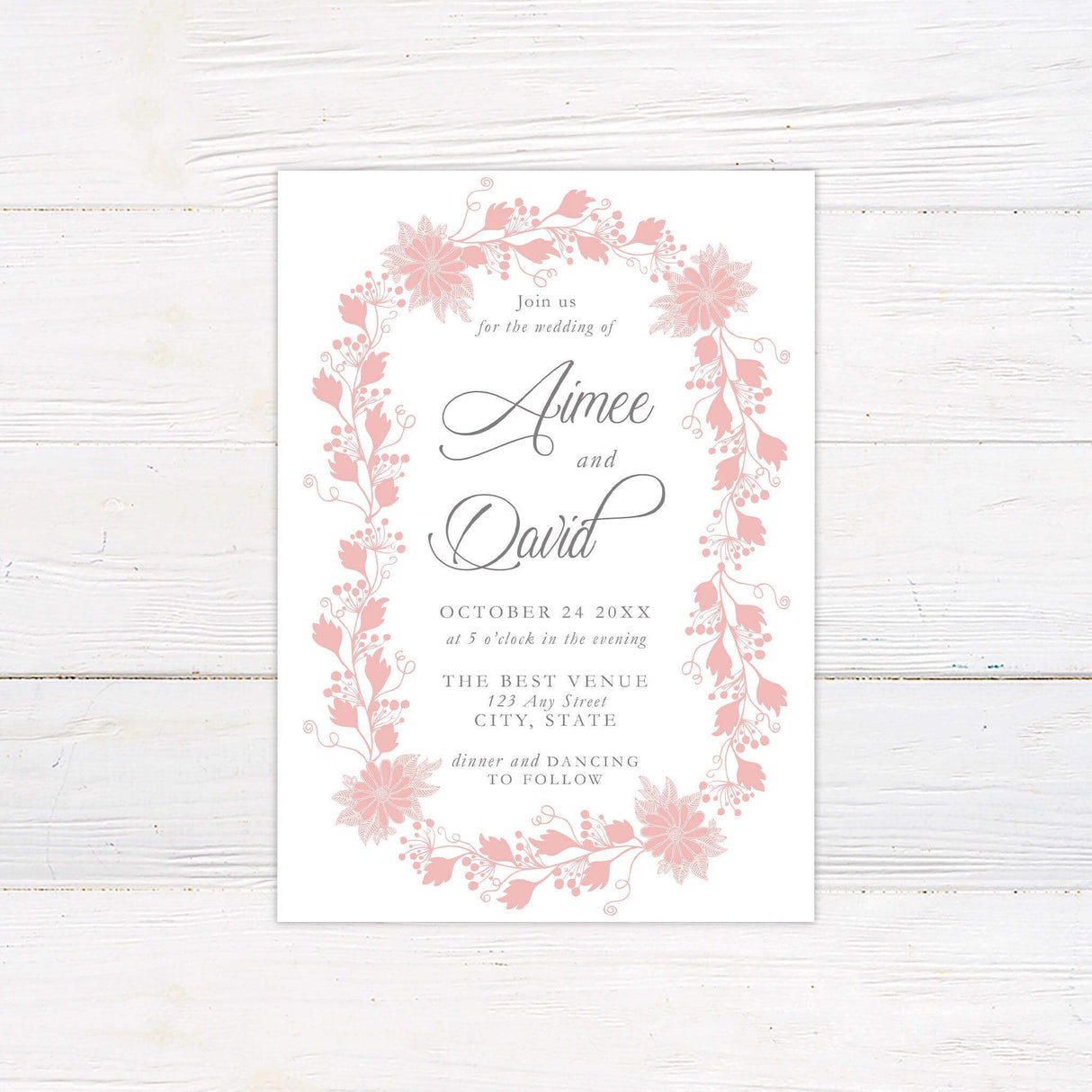 Romantic pink floral wreath wedding invitation with elegant script and serif text, featuring hand-drawn botanical elements in an oval frame.