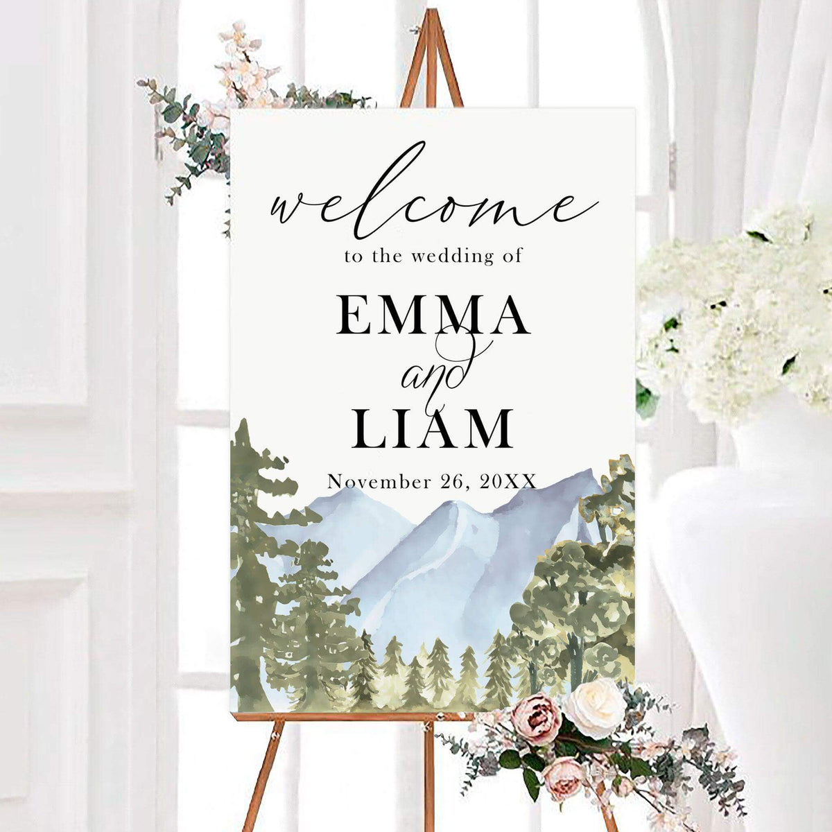 Watercolor forest wedding welcome sign featuring evergreen trees and scenic blue mountain peaks. Elegant lettering displays the couple’s names and personalized wedding date.