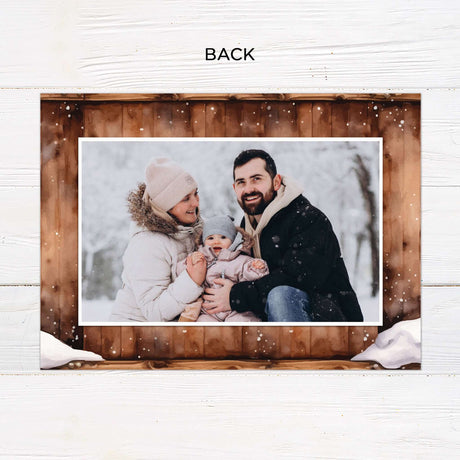 This gatefold holiday card features a cozy woodgrain background with a snow-dusted edge and watercolor floral wreath. Inside, it displays framed photos, festive typography with “Wishing You a Merry Christmas and a Happy New Year,” and a monogram accent. - back.