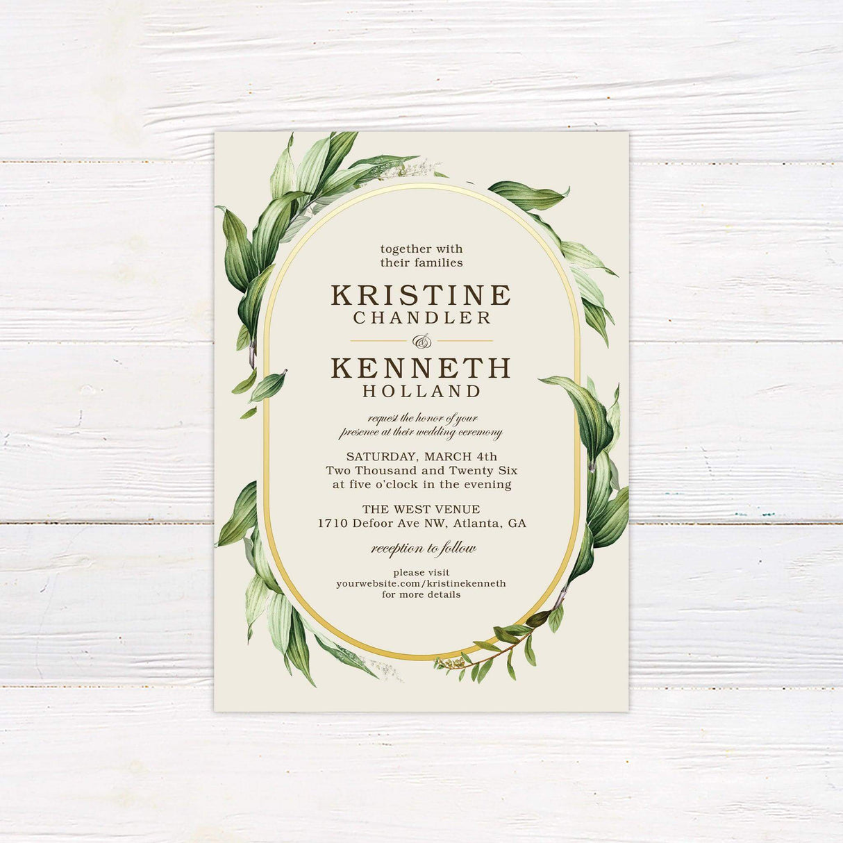 Elegant wedding invitation with gold oval frame and watercolor greenery leaves on a soft cream background