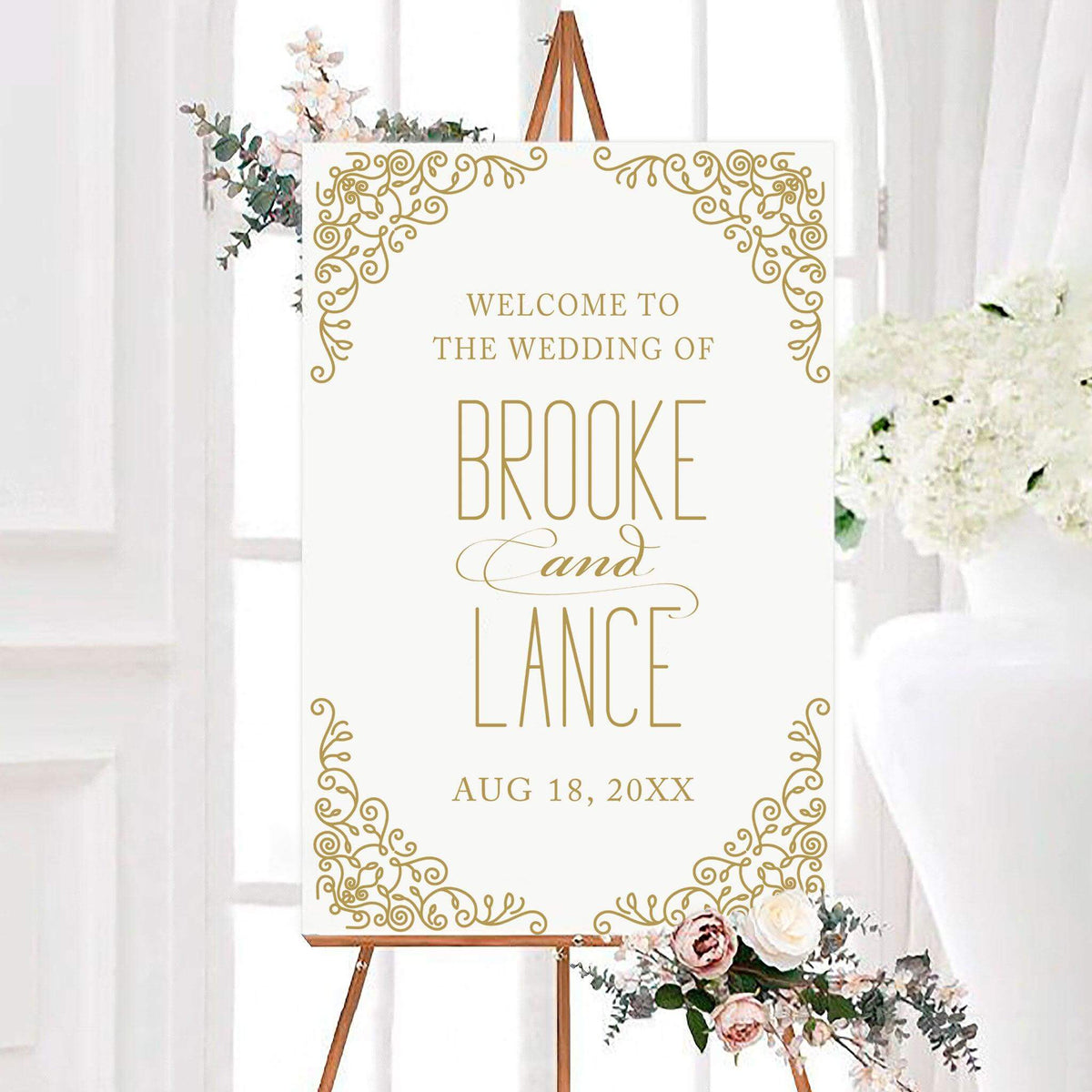 Personalized gold fringe wedding welcome sign featuring ornate scrolling flourishes in each corner and elegant typography. The couple’s names and wedding date are displayed prominently in the center.