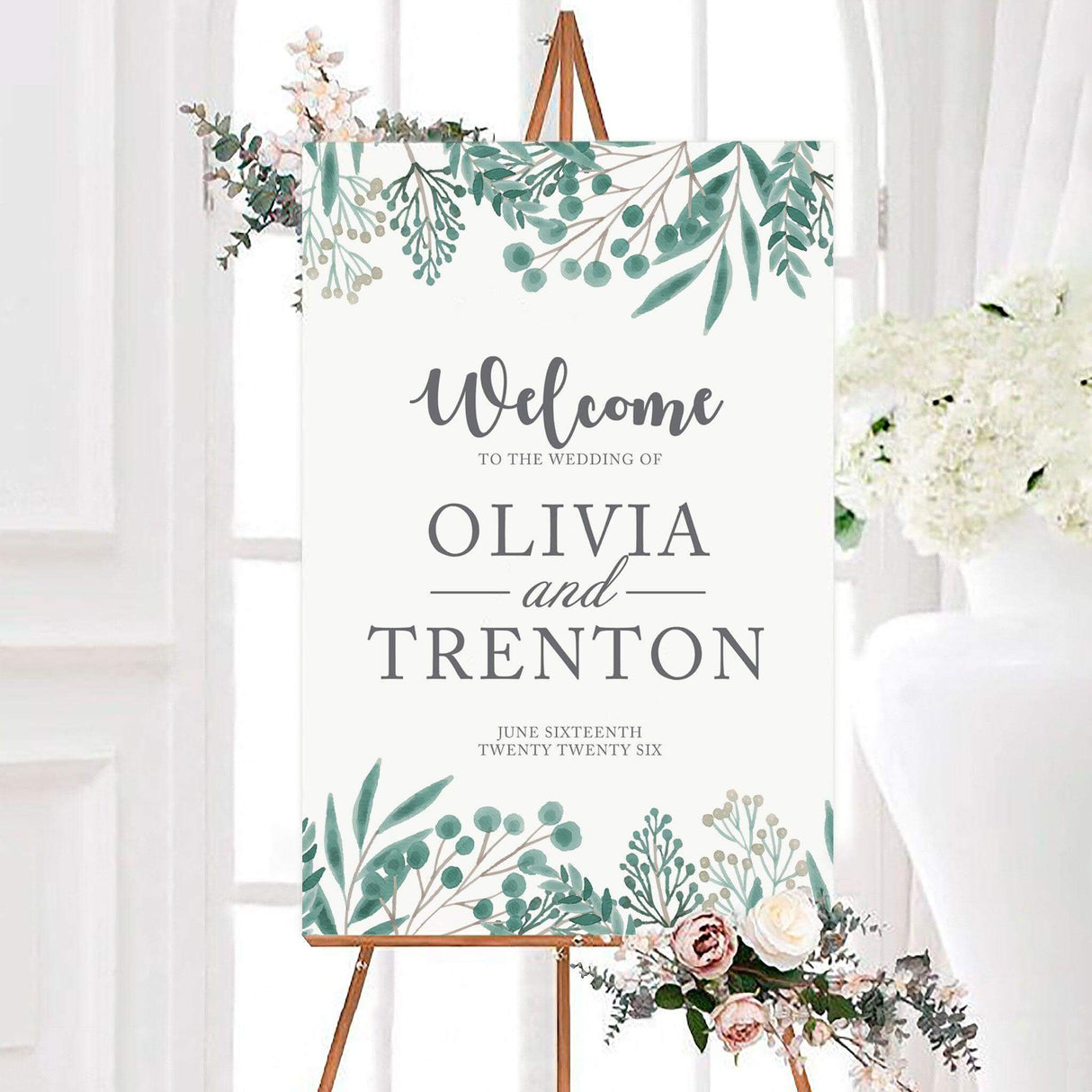 Personalized green botanical wedding welcome sign featuring watercolor green botanical leaves, branches, and berries around a white background. Elegant script and serif lettering display the couple’s names and wedding date.