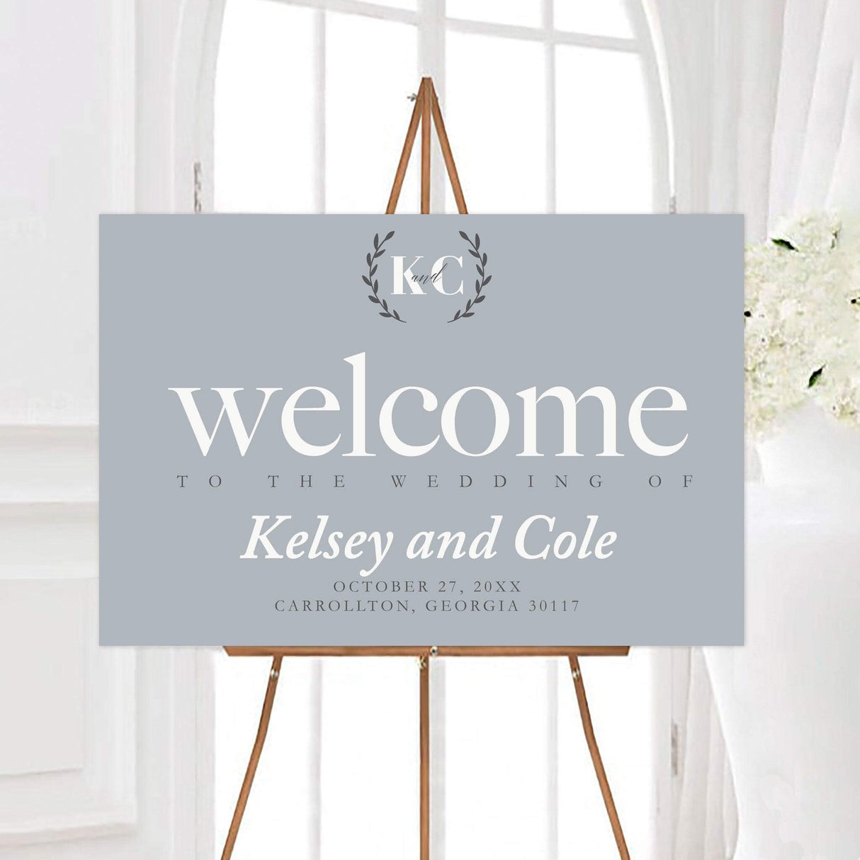 Minimal grey simple wedding welcome sign featuring oversized typography and a personalized monogram surrounded by a simple leafy wreath. The clean design includes the couple’s names, wedding date, and event details on a soft neutral background.