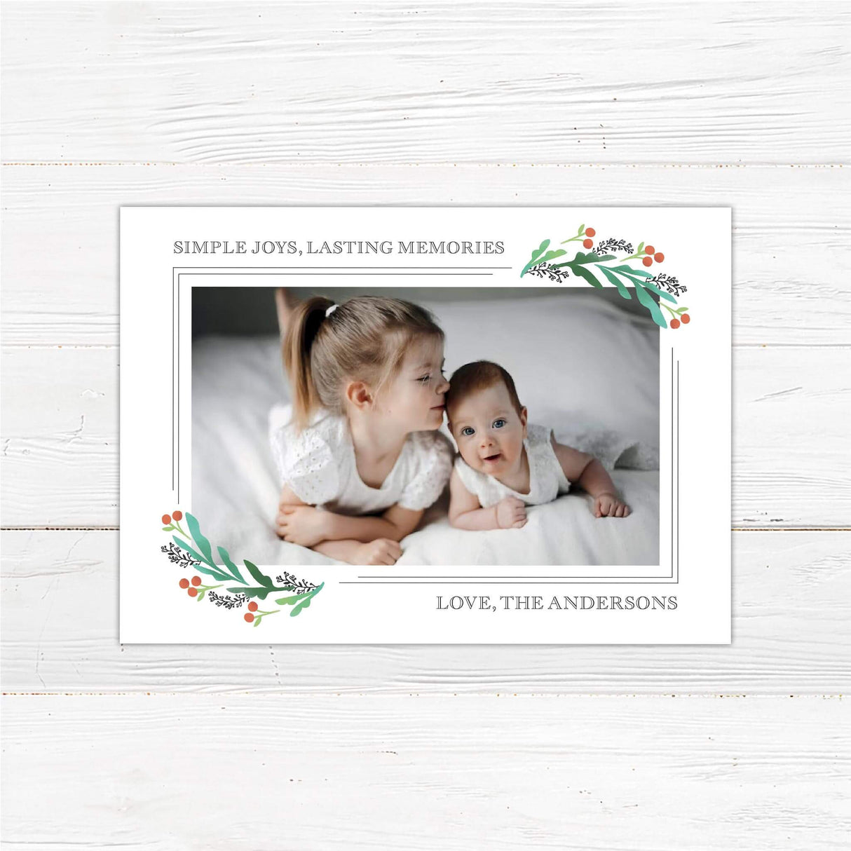 Holiday photo card featuring two children with soft watercolor holly berry corners and text reading