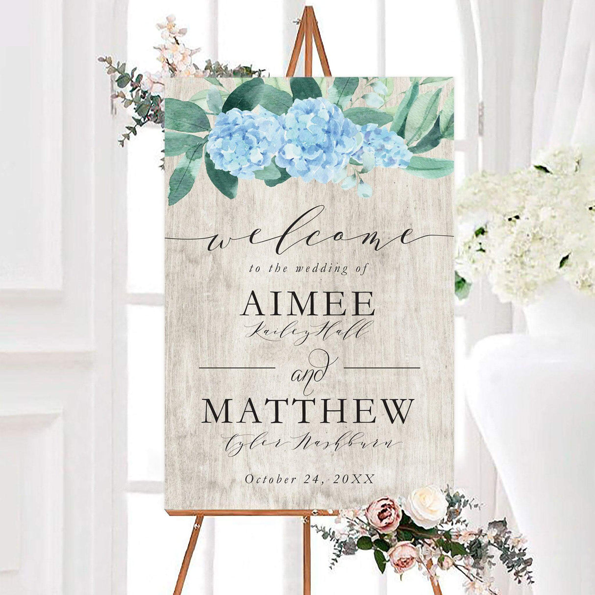 Hydrangea wood wedding welcome sign featuring watercolor blue hydrangeas and green foliage on a rustic wood-inspired background. The personalized design includes the couple's names and wedding date in elegant black typography.