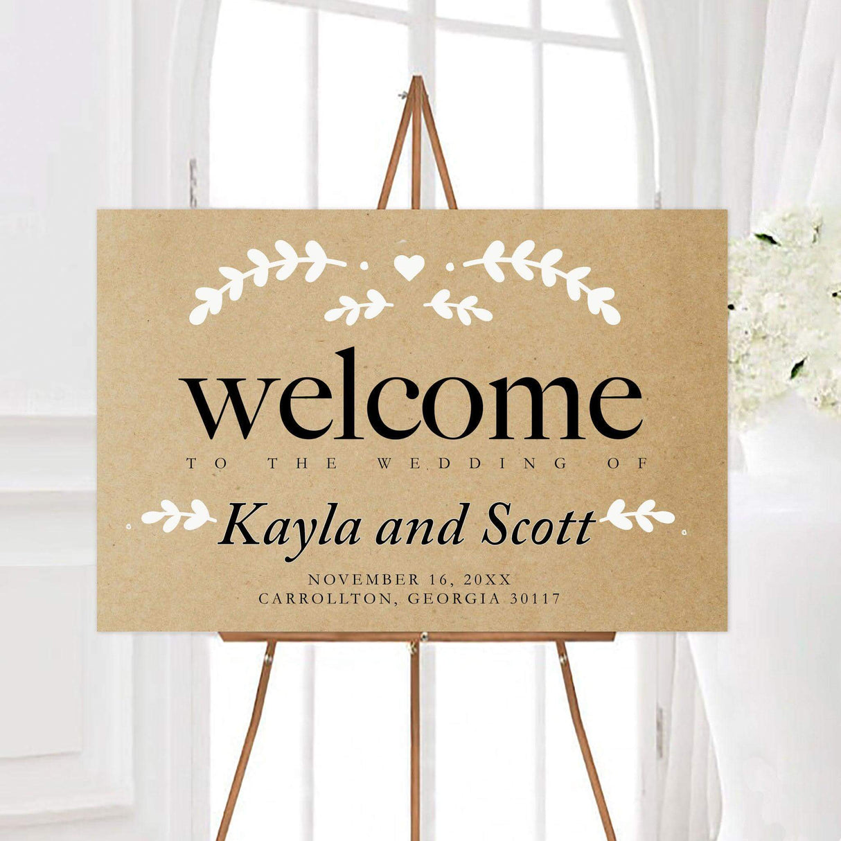 Kraft and white wedding welcome sign featuring a kraft-inspired background, black personalized typography, and white leafy branch accents with a small heart. The rustic botanical design creates a warm greeting for wedding guests.