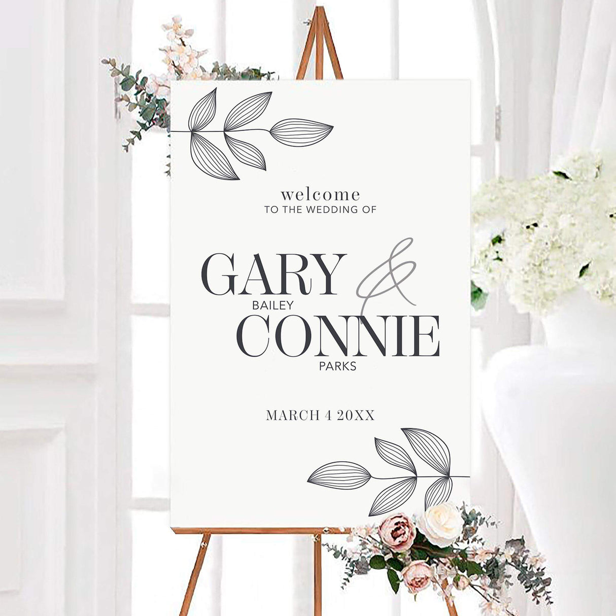 Minimalist leaf imprint wedding welcome sign with hand-drawn charcoal leaf branches, elegant serif names, and a large flowing ampersand. The personalized botanical design includes the couple’s surnames and wedding date on a white background.