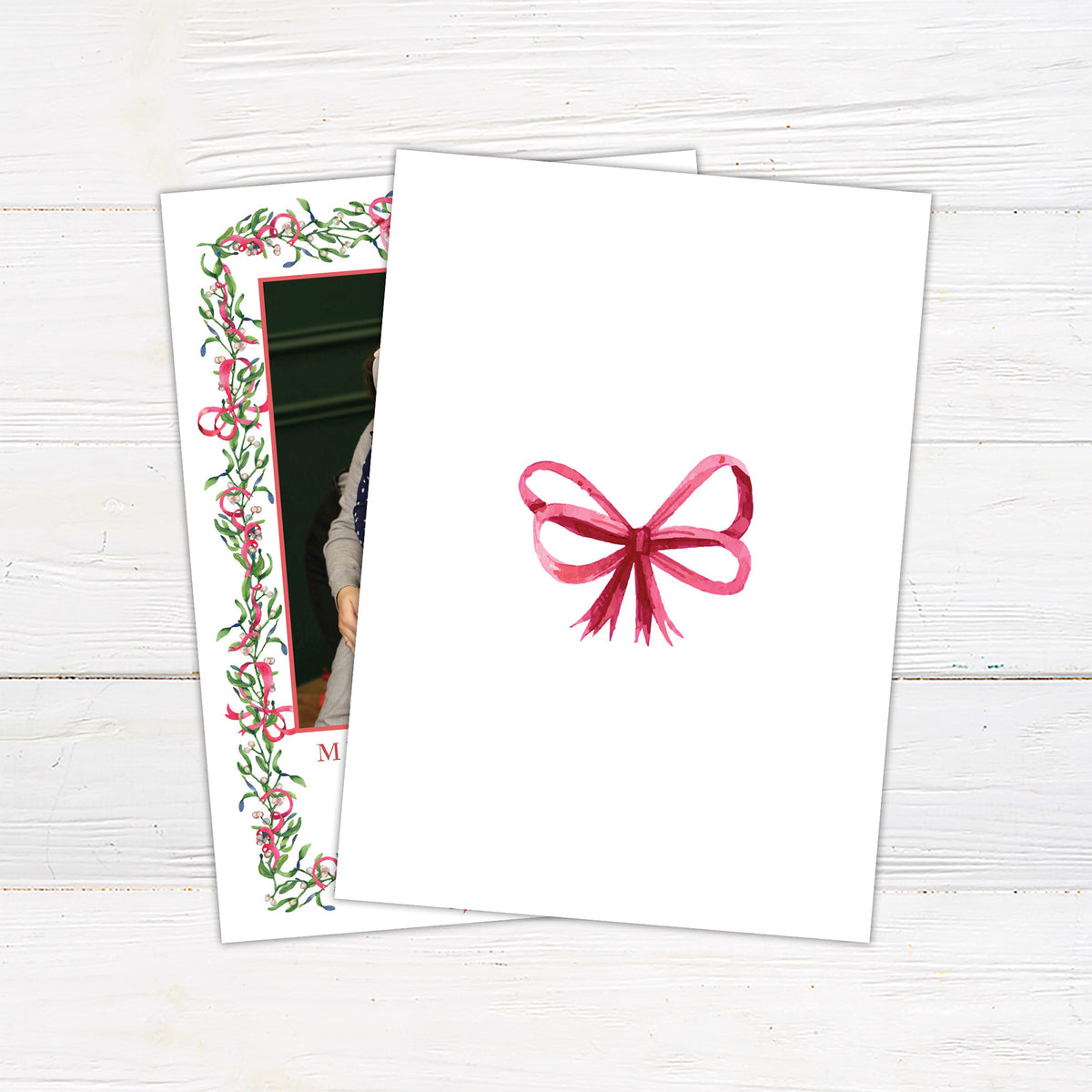 Personalized Christmas photo card featuring a family portrait framed by watercolor mistletoe, greenery, berries, and ribbon bows. The back features a coordinating watercolor bow.