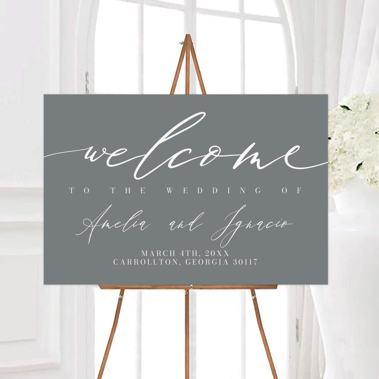 Minimalist gray script wedding welcome sign with elegant white script lettering and personalized couple names. The design includes the wedding date and location in classic white typography.